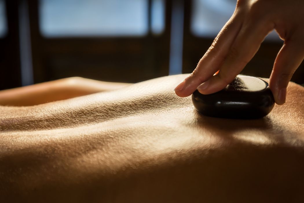 Aesthetician placing hot stones along a client’s back during a relaxing hot stone massage, a popular service add-on at Namaste Skincare & Wellness.